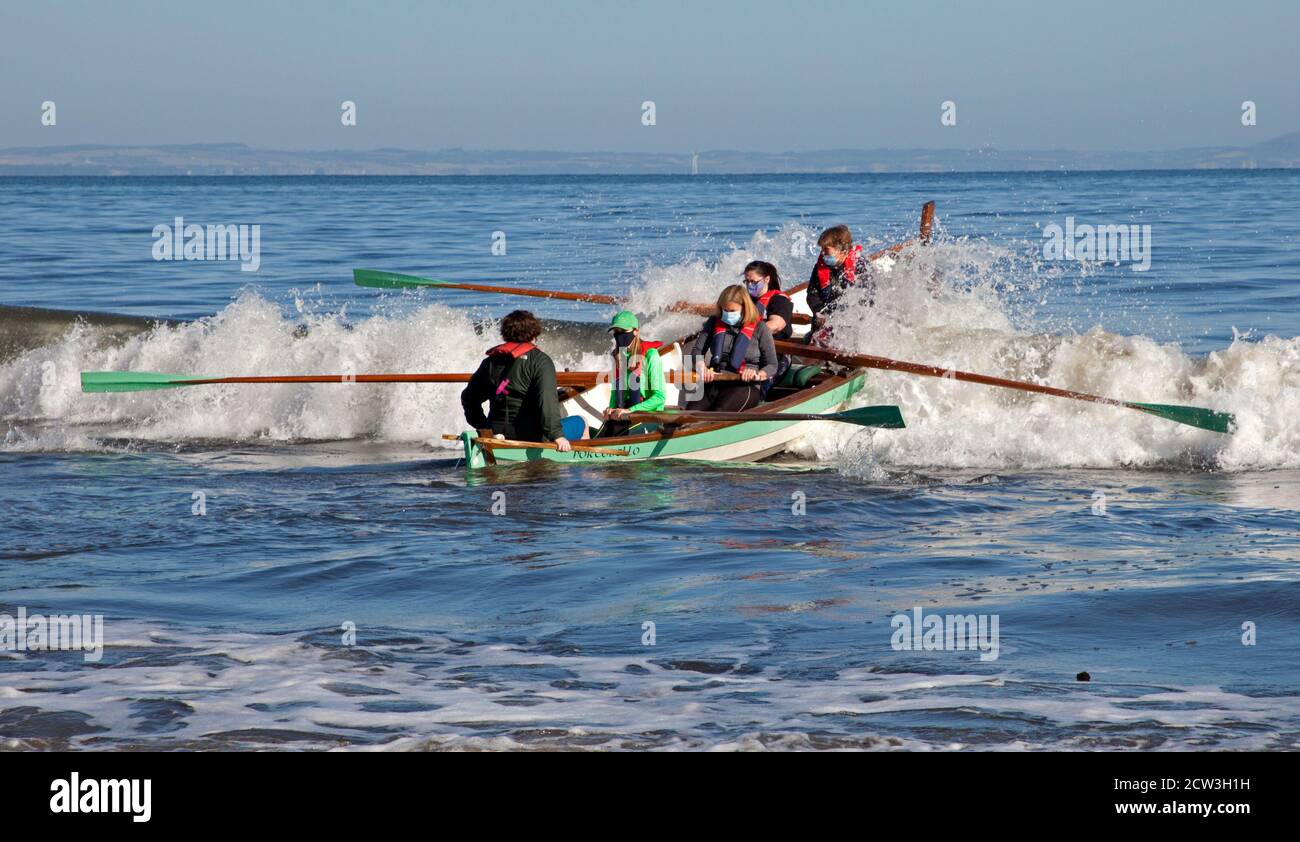 Portobello, Edinburgh, Scotland, UK. 27 September 2020. Temperature 4 degrees after a cold night and  morning, a dramatic skilled launch into the Firth of Forth for the Row Porty team. After a six month layoff due to the Covid-19, Coronavirus pandemic it is obvious this masked crew have not lost their rowing skills. Stock Photo