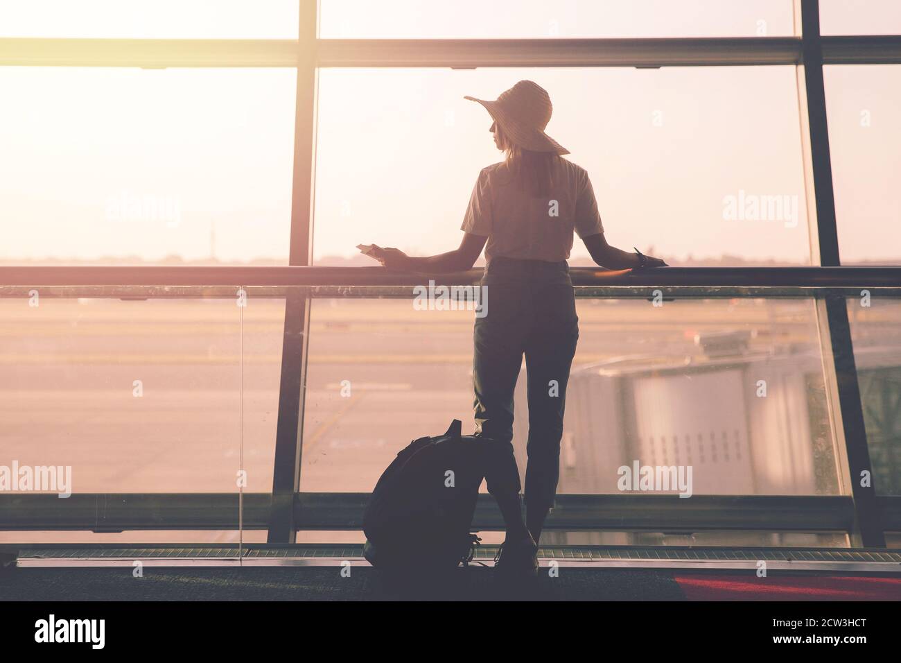 Airport, woman travel with hand luggage waiting for plane in terminal on background of transparent windows Stock Photo