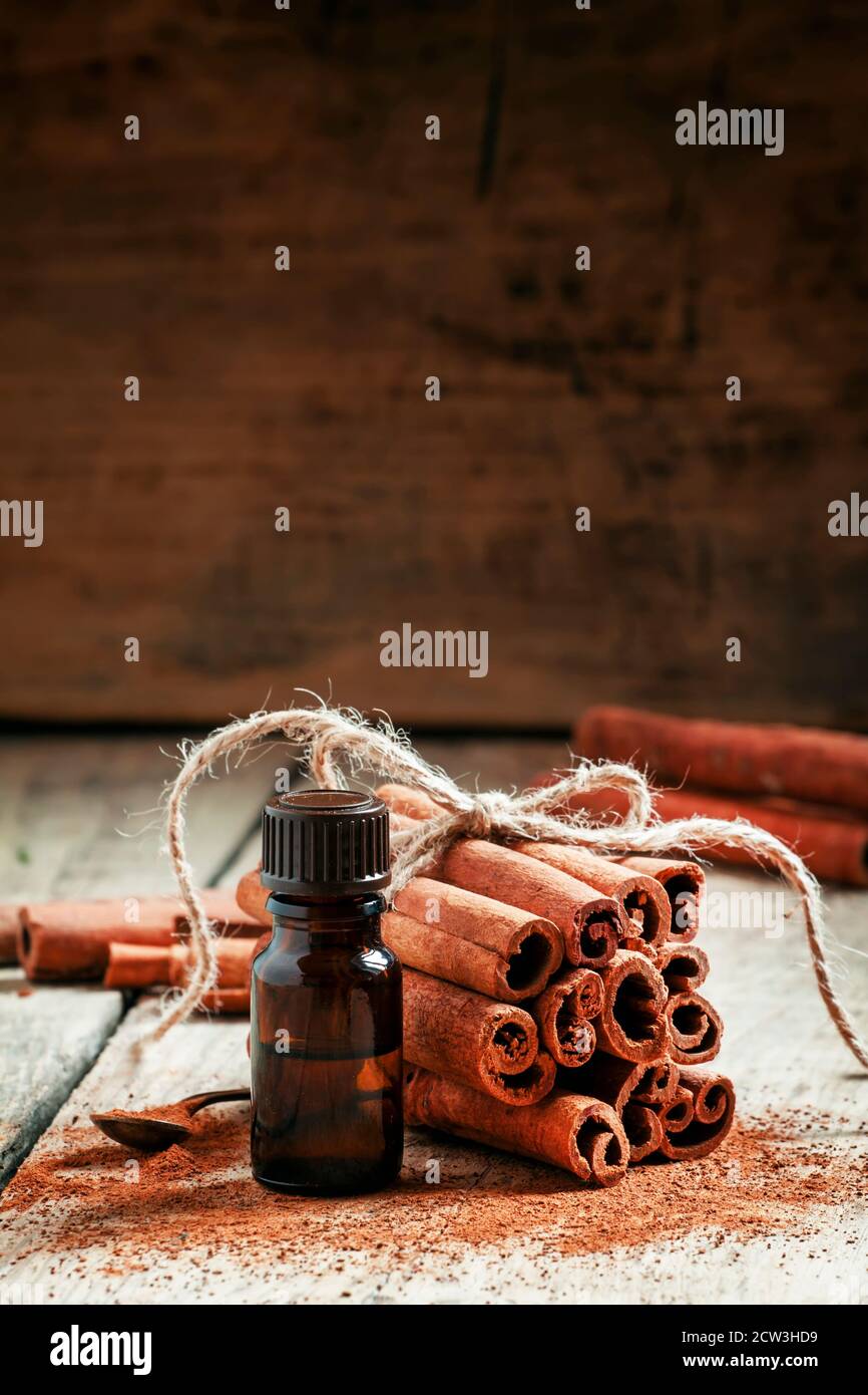 Essential cinnamon oil in a small bottle, ground cinnamon and cinnamon sticks on old wooden background, selective focus Stock Photo