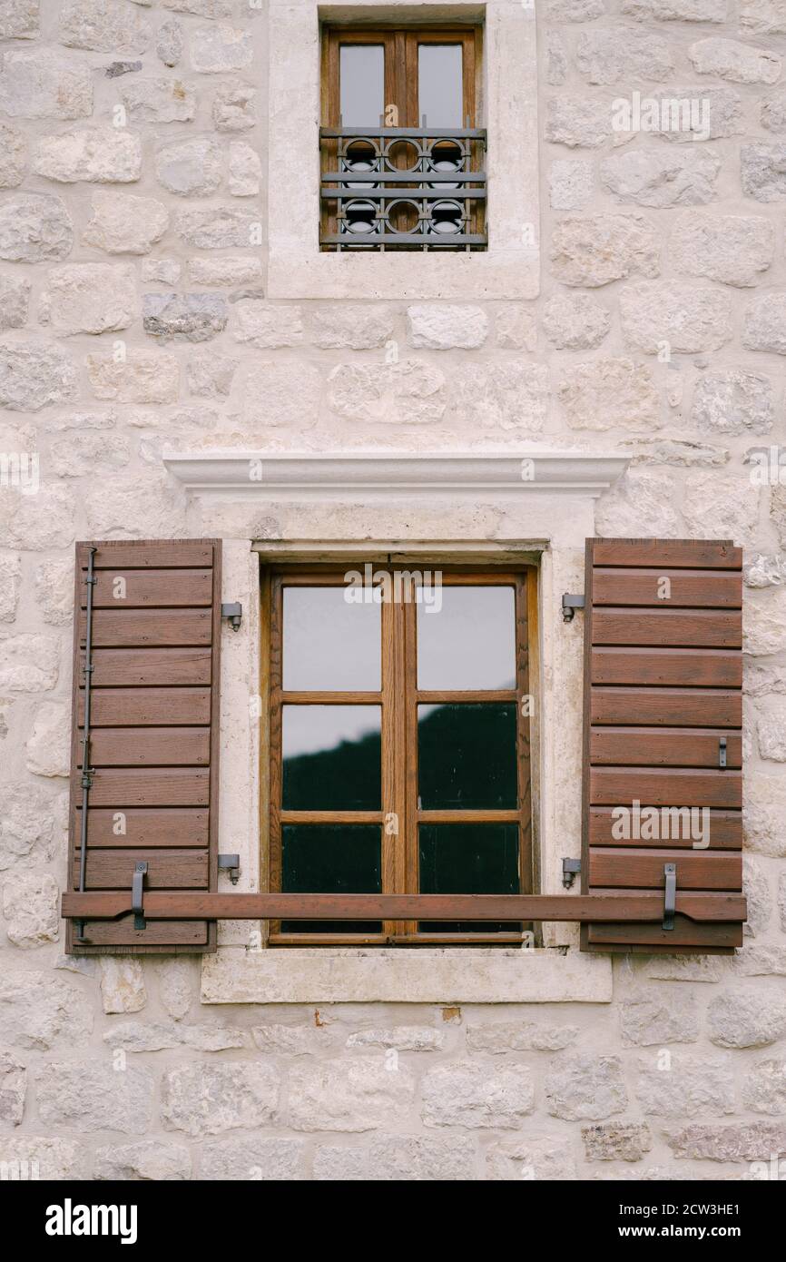 A brown window with wooden shutters and a small window with metal bars on a white wall. Stock Photo