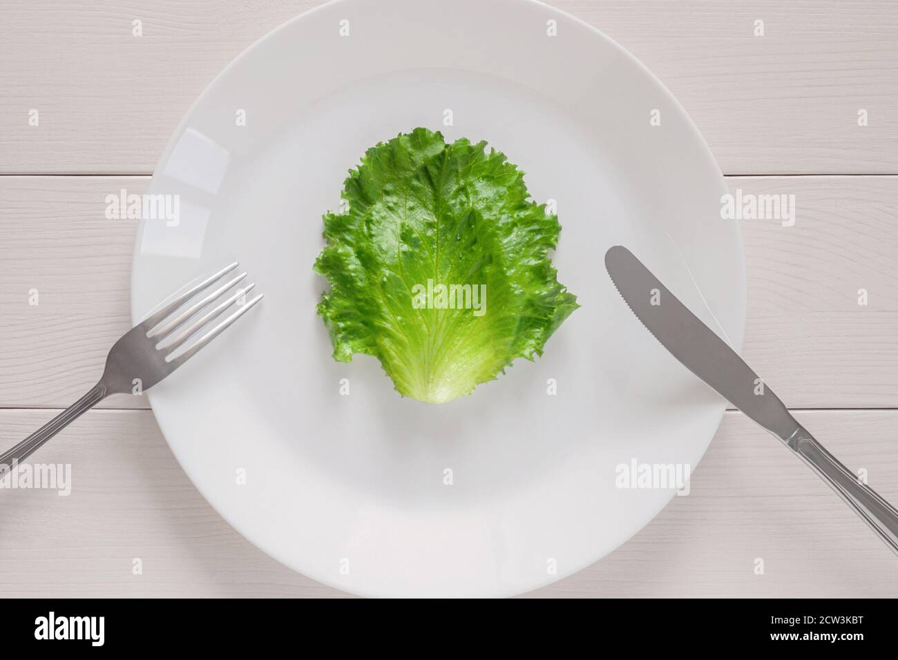 leaf lettuce on white plate with fork and knife, top view on wooden table Stock Photo