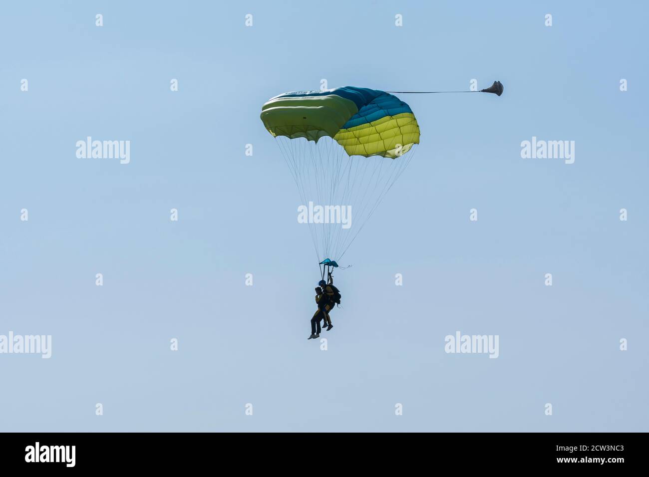 Tandem parachute jump. Silhouette of skydiver flying in blue clear sky. Concepts of extreme sport and adrenaline. Stock Photo