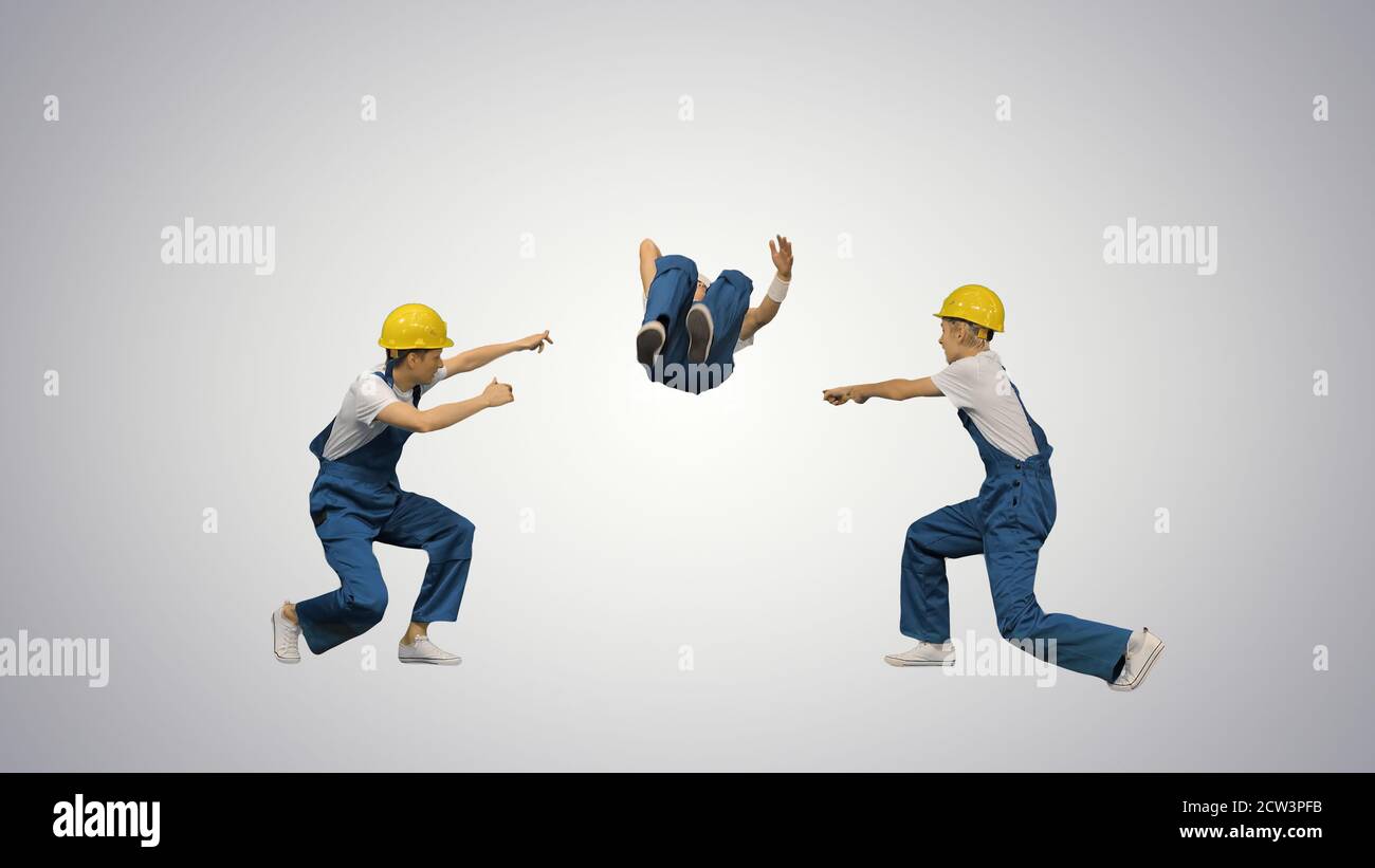 Three young construction workers in hard hats synch dancing look Stock Photo