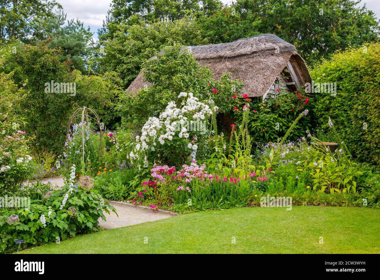 A colourful herbaceous border and thatched cottage in the Cottage Garden at RHS Rosemoor, Great Torrington, Devon, England, UK Stock Photo