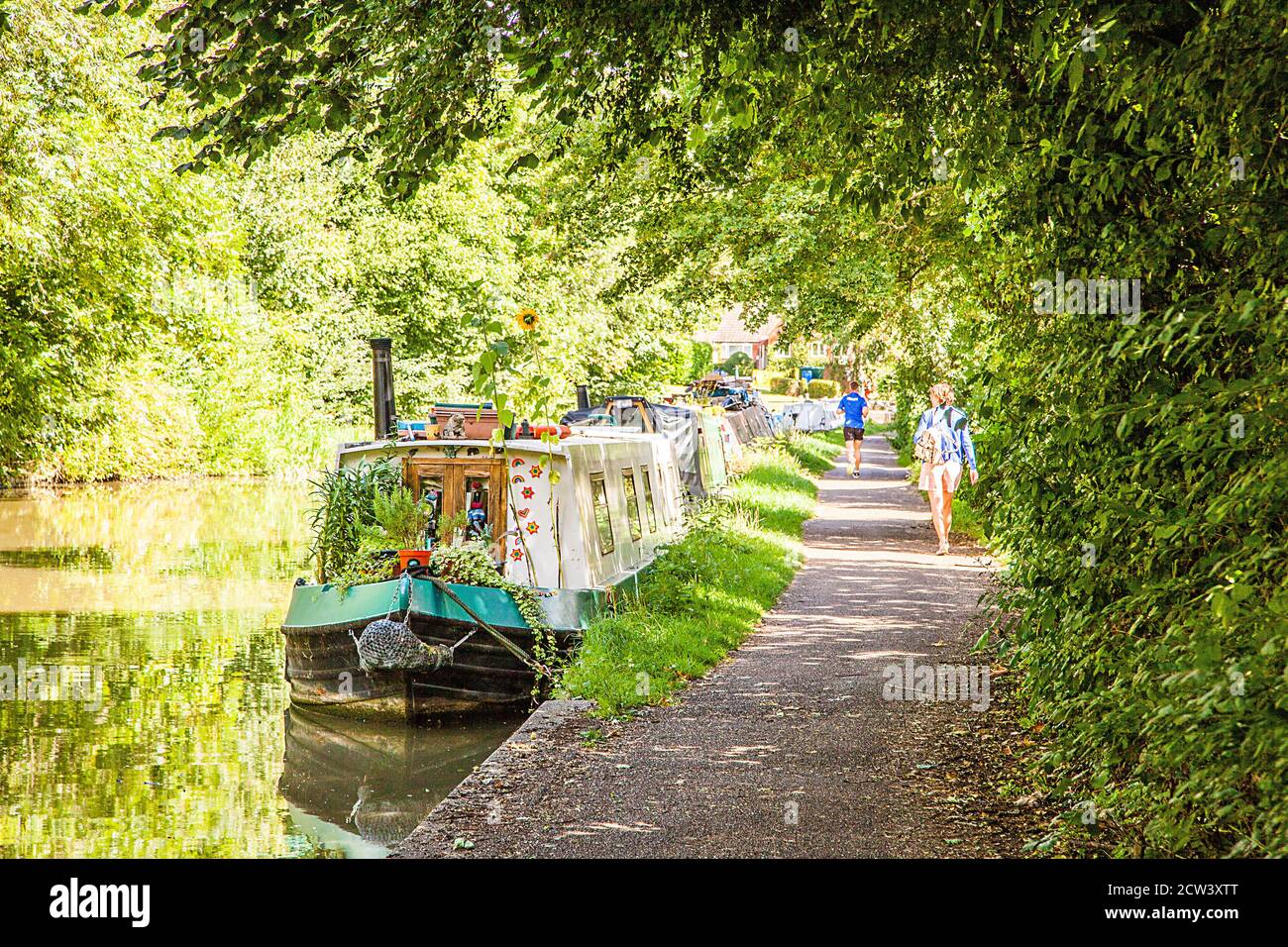 Woman walking along the towpath  past canal narrowboats on the Grand Union canal at Linslade Leighton Buzzard Bedfordshire England Stock Photo