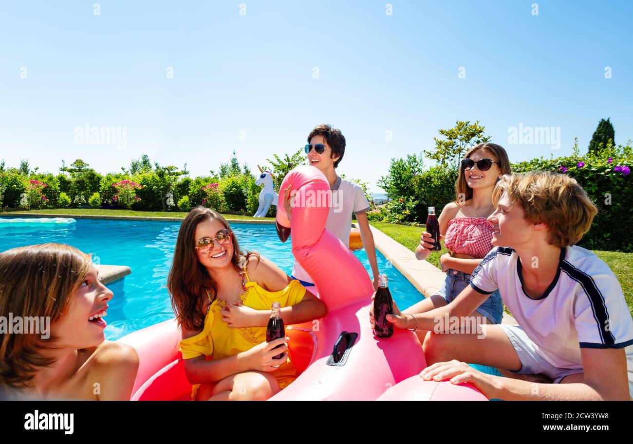 Many teenage boys and girls chat, drink soda celebrating sitting on the border pool with inflatable buoys Stock Photo