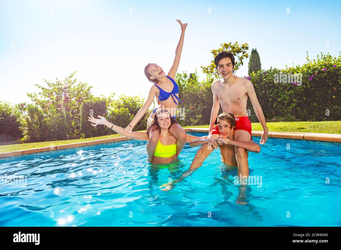 Children carry each other on shoulders standing together in the pool with  friends smiling and wave hands Stock Photo - Alamy