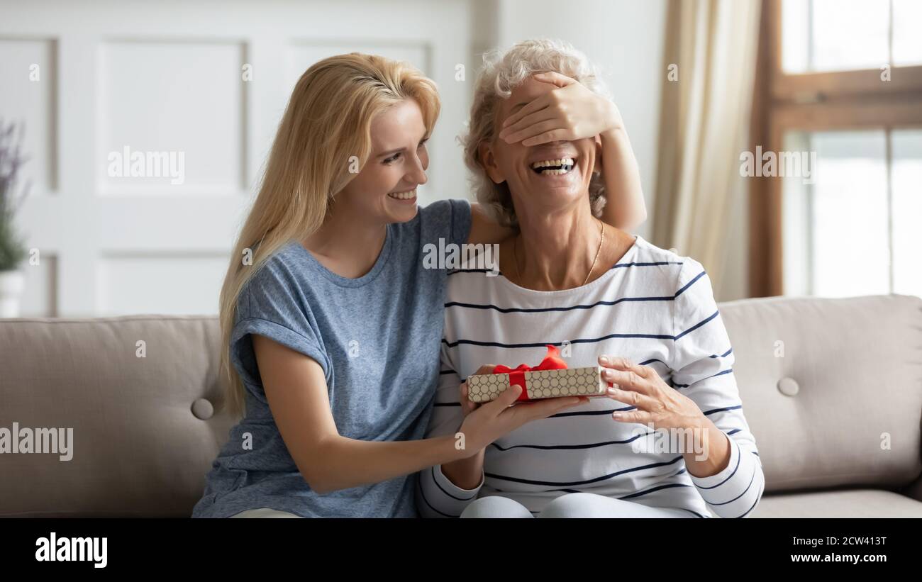 Laughing grownup daughter congratulates mature mother giving her birthday surprise Stock Photo