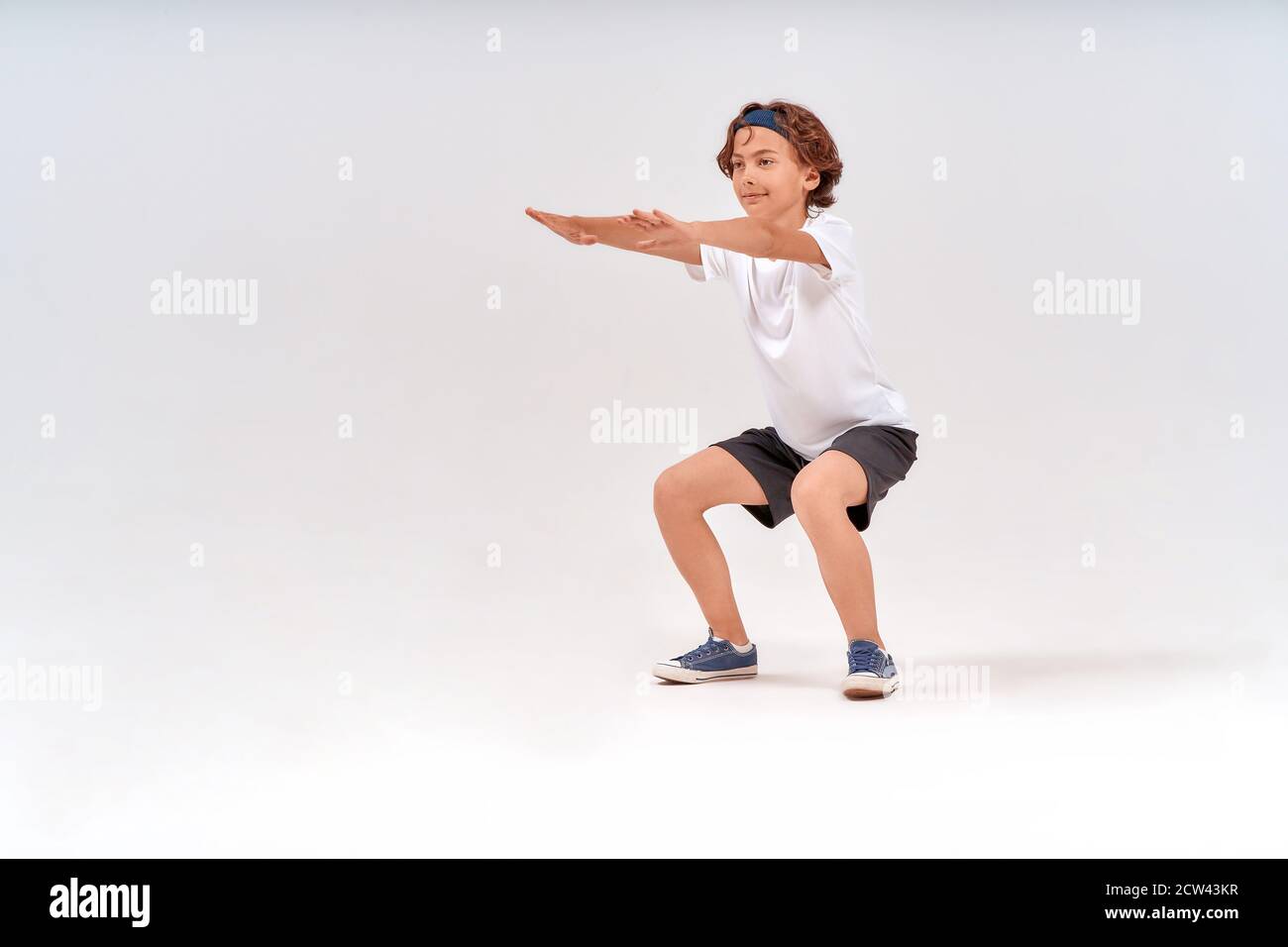 physical activities. Full length of caucasian teenage boy in sportswear squatting, doing sit-ups isolated over grey background in studio Stock Photo