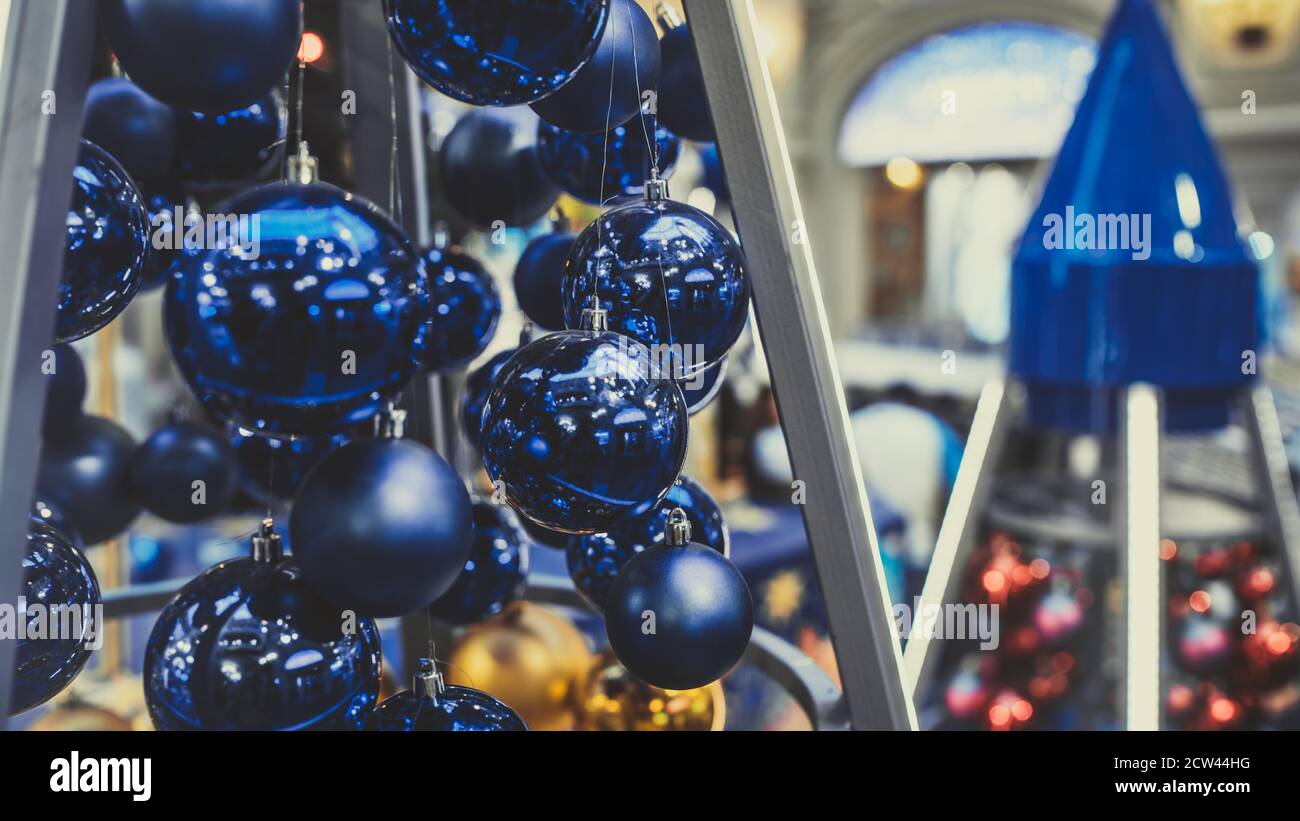 Close up of christmas toys suspended on metal construction in hall in shopping center. Blue christmas balls hanging on strings for room decoration and Stock Photo