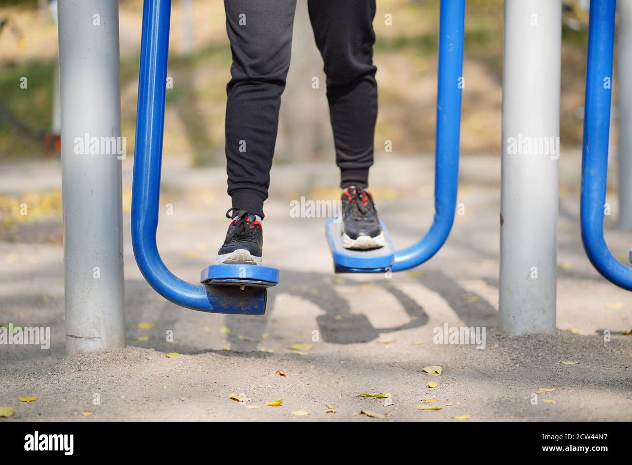 Portrait of woman's legs on street simulator in park. Close up of body part of female doing sports on athletic field in autumn season Stock Photo