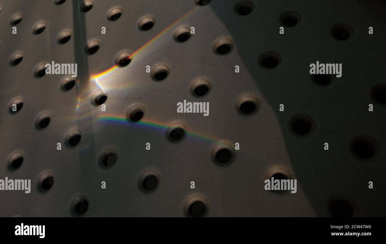 Sun flare of rainbow spectrum light on dotted surface with abstract shadows. Circle hole pattern background Stock Photo