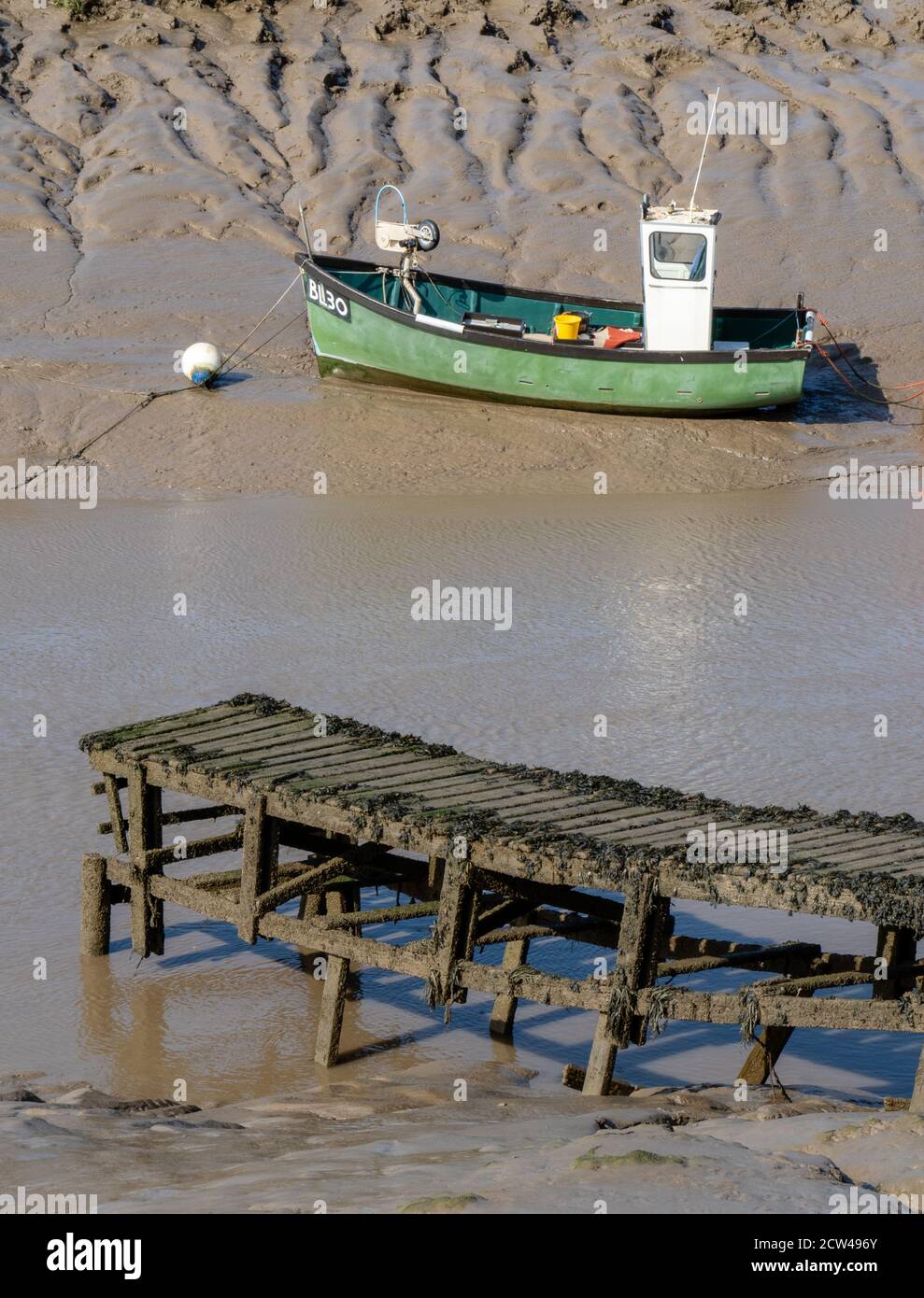 Pea green fishing boat moored on the muddy banks of the River Axe near Weston super Mare in Somerset UK Stock Photo