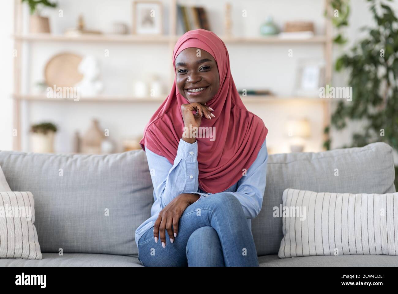Joyful young african muslim woman in hijab posing on couch at home ...