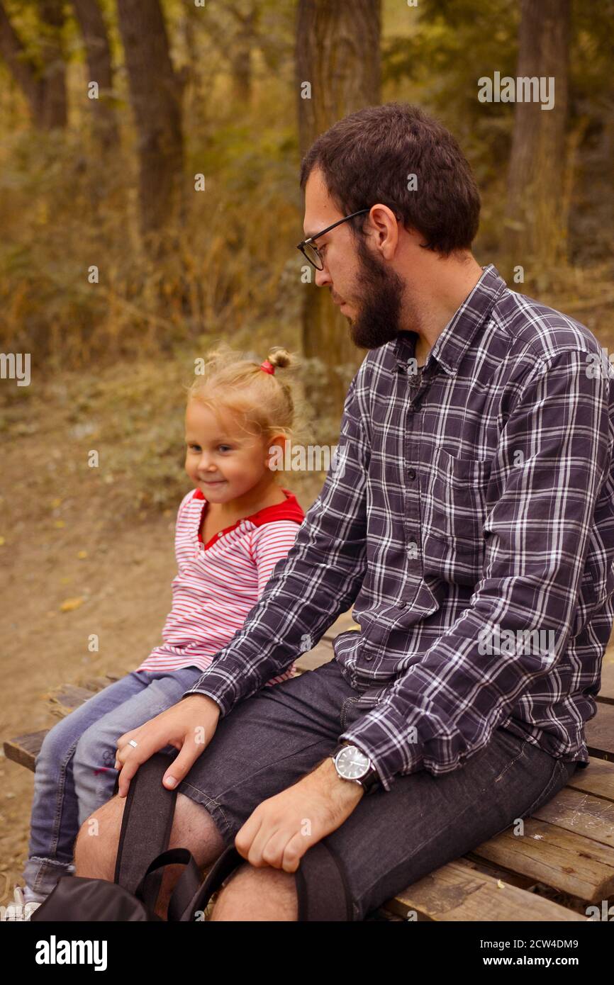 Baby and father are playing in the autumn park. Dad and daughter are sitting on a wooden bridge outdoors. Happy family moments of childhood. Stock Photo