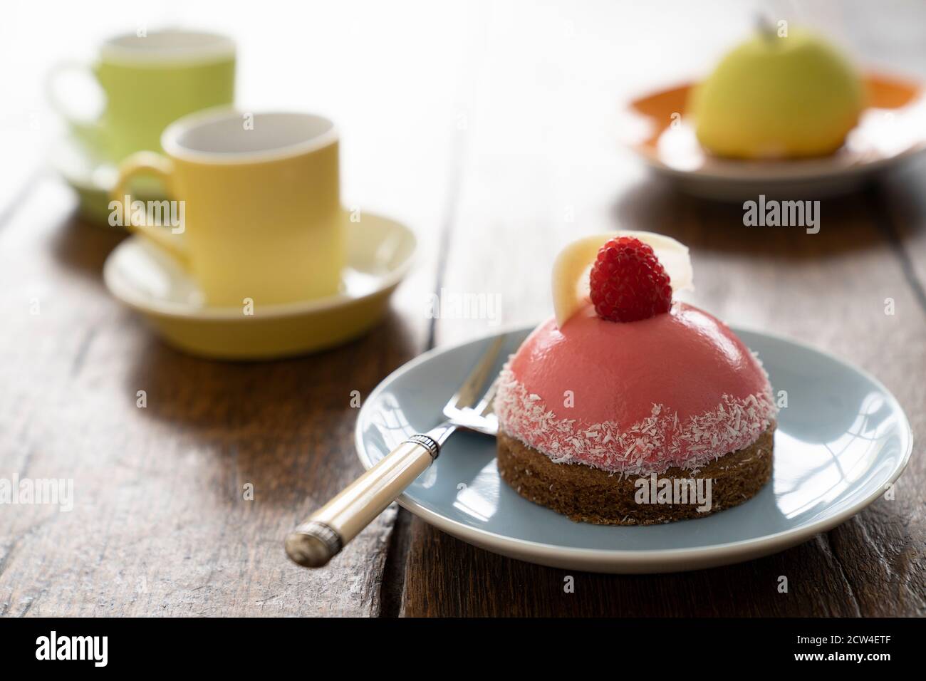 Two Small French ball shaped cakes mousse dome served on a plate with cups of tea Stock Photo