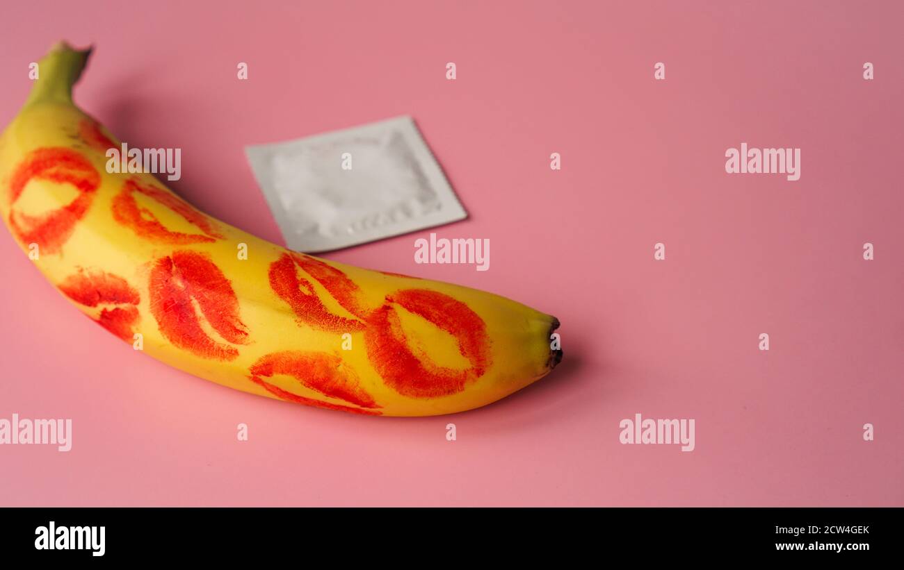 Unpacked condom and red lipstick on a yellow banana on pink studio background. Contraceptives, prevention of venereal disease, preventing pregnancy Stock Photo