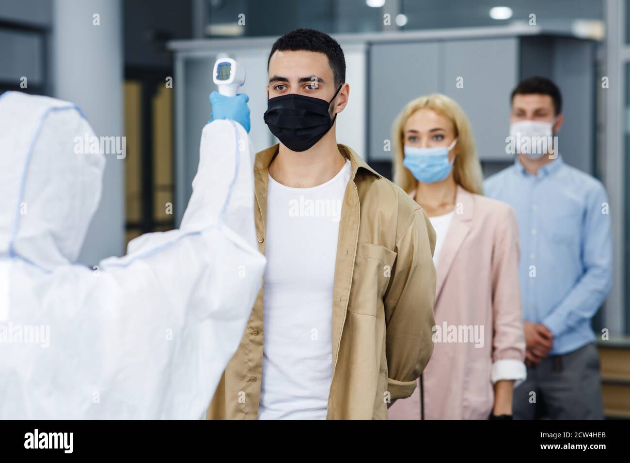 New normal and coronavirus disease control. Medic in protective uniform with infrared thermometer to measure temperature of workers Stock Photo