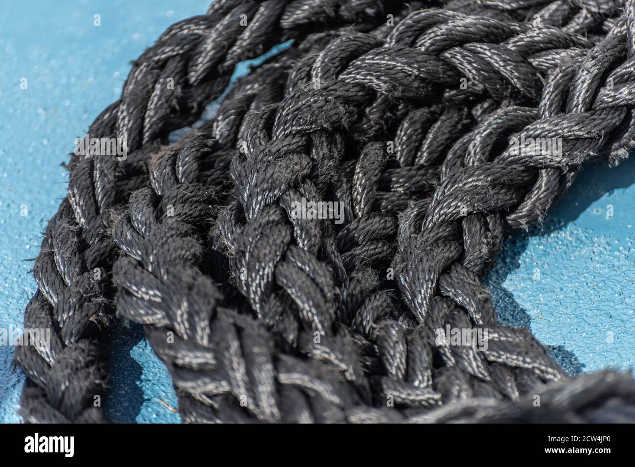 Thick, black rope on a blue ship deck Stock Photo
