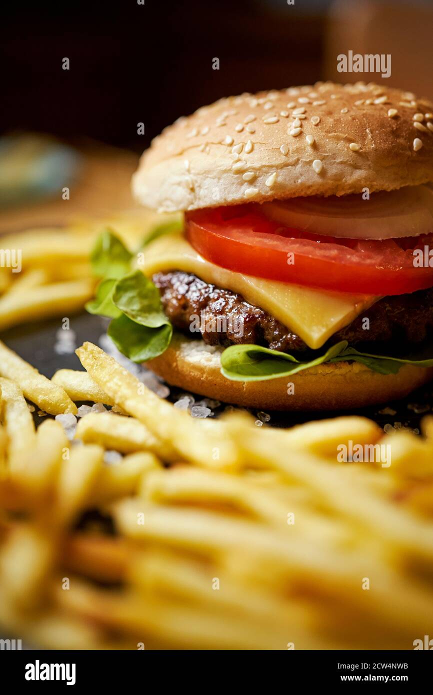 cheeseburger surrounded by french fries on a black table Stock Photo