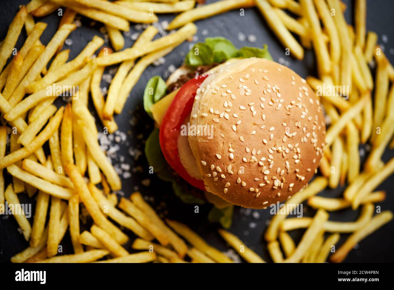 cheeseburger surrounded by french fries on a black table Stock Photo