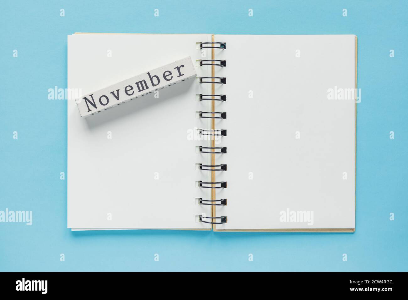 Clean spiral note book for notes and messages and november wooden calendar bar on blue background. Minimal business flat lay Stock Photo