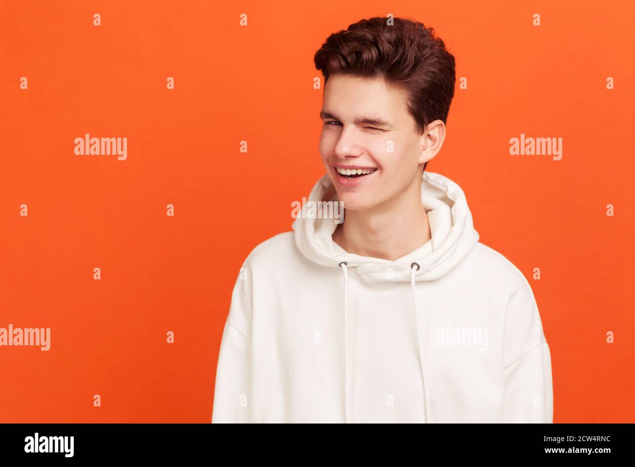 Handsome guy in white sweater with stylish hairdo winking and optimistically smiling, good mood. Cunning boy flirting. Indoor studio shot isolated on Stock Photo