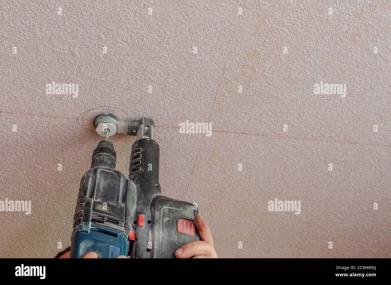 A man holds a power drill in his hands. Make a hole in the ceiling. Repair work in the apartment. Restoration indoors. Stock Photo