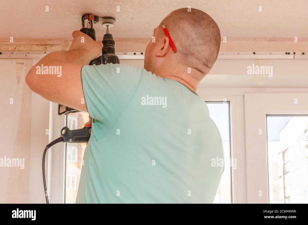 A man holds a power drill in his hands. Make a hole in the ceiling. Repair work in the apartment. Restoration indoors. Stock Photo