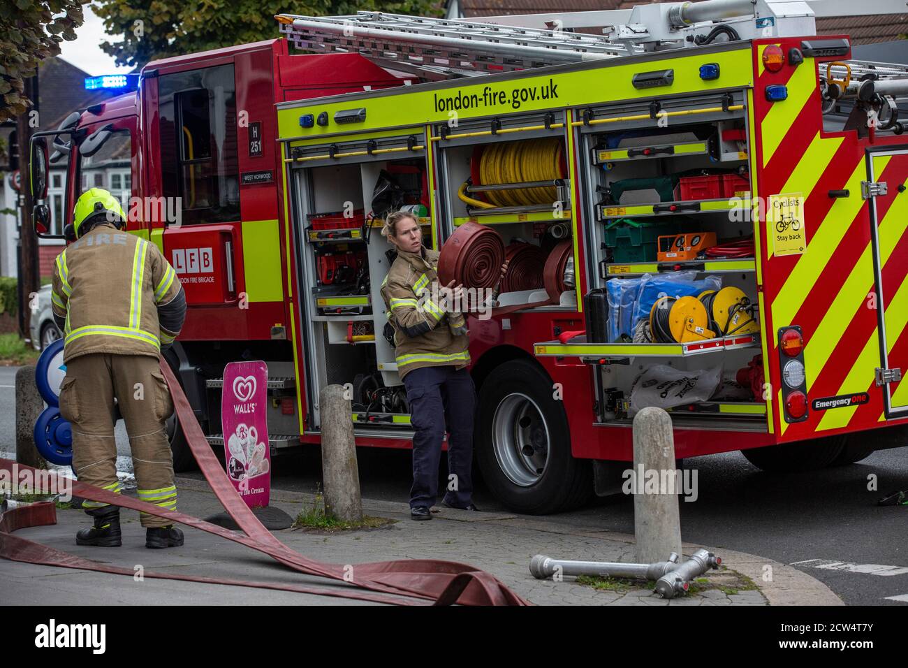 Woman Firefighter rolls out the hose with London Fire Brigade attending a house fire in a residential street, South London, England, United Kingdom Stock Photo