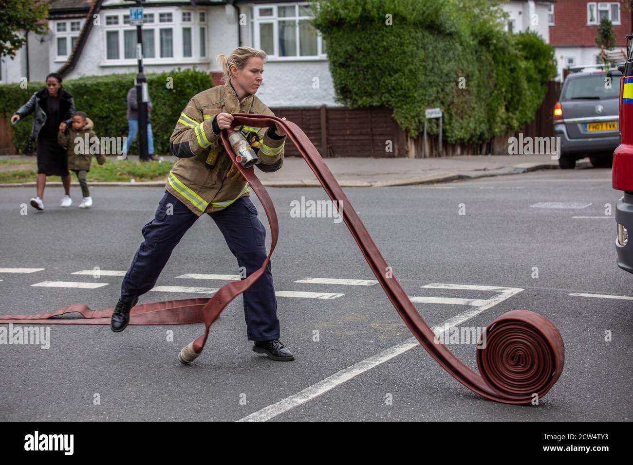 Woman Firefighter rolls out the hose with London Fire Brigade attending a house fire in a residential street, South London, England, United Kingdom Stock Photo