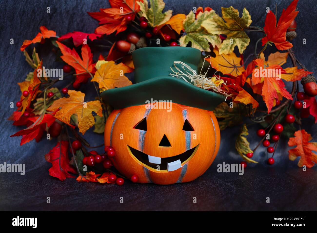 Artificial Orange Halloween Pumpkin with Green Hat. Artificial Autumn Leaves. Halloween and Fall Vibes. Stock Photo