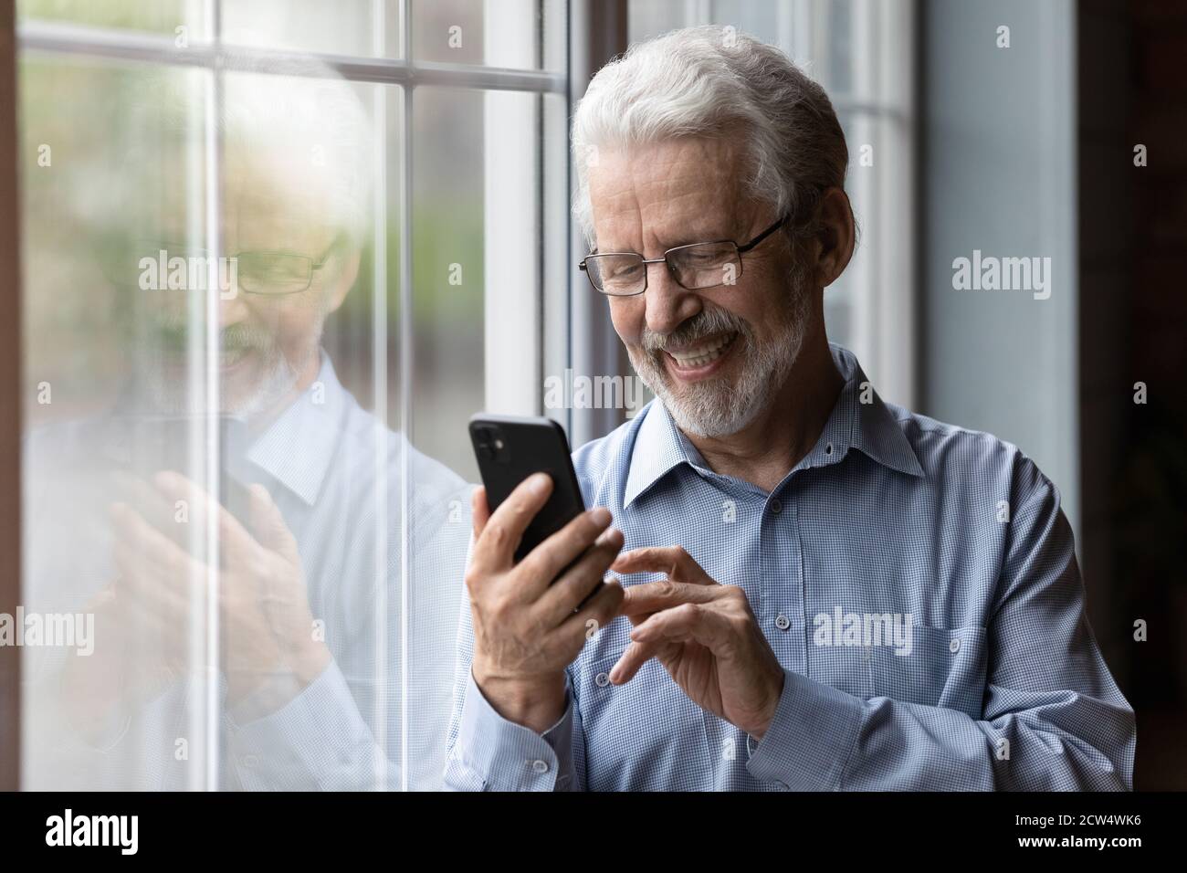 Smiling mature man using modern smartphone at home Stock Photo