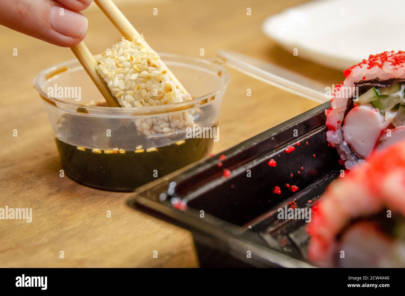 Holding sushi covered with sesame with wooden chopsticks to dip in soy sauce on a wooden table Stock Photo