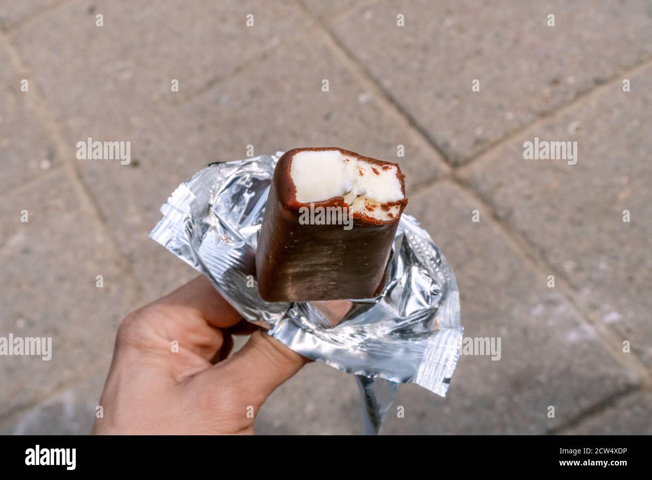 The hand of a man holding a white ice cream covered with chocolate in a wrapper on the background of the plates Stock Photo