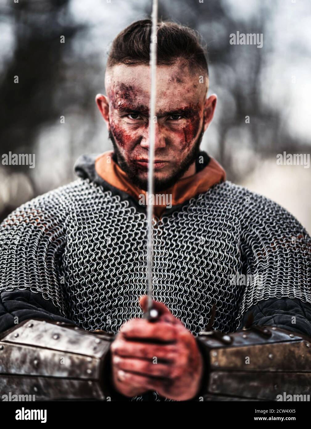 Young strong man in a medieval warrior costume holds a sword in