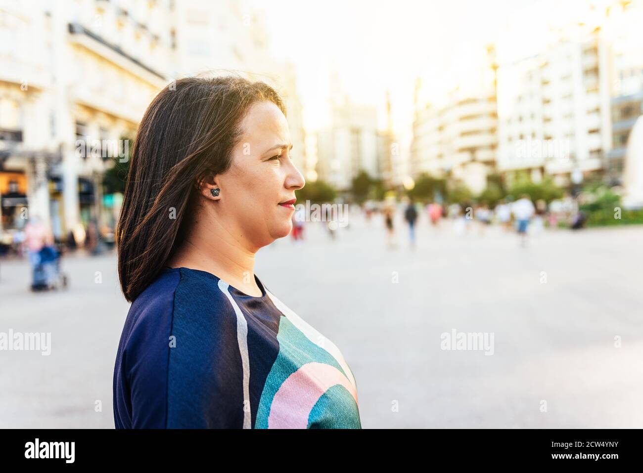 Middle-aged brunette woman side face in a square in Europe at sunset. copy space Stock Photo