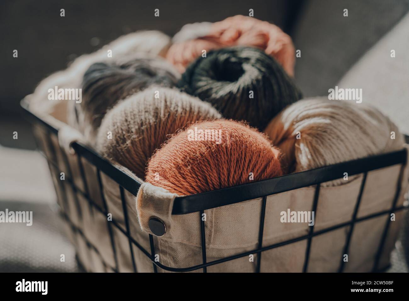 Close up of balls of earth coloured yarn inside a basket, sunlight from the window on it, selective focus. Stock Photo