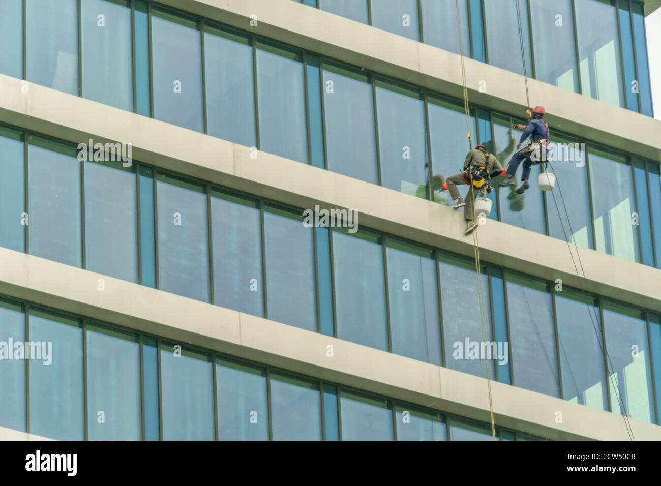 Two workers are washing the windows of a high-rise glass building. Work ...