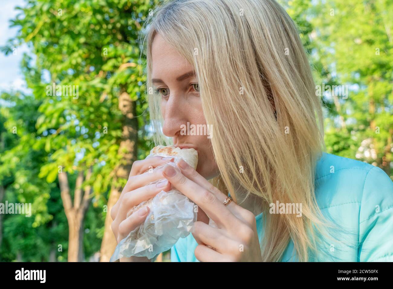 Blonde girl eating shawarma outside on a sunny spring day. Fast food Stock Photo