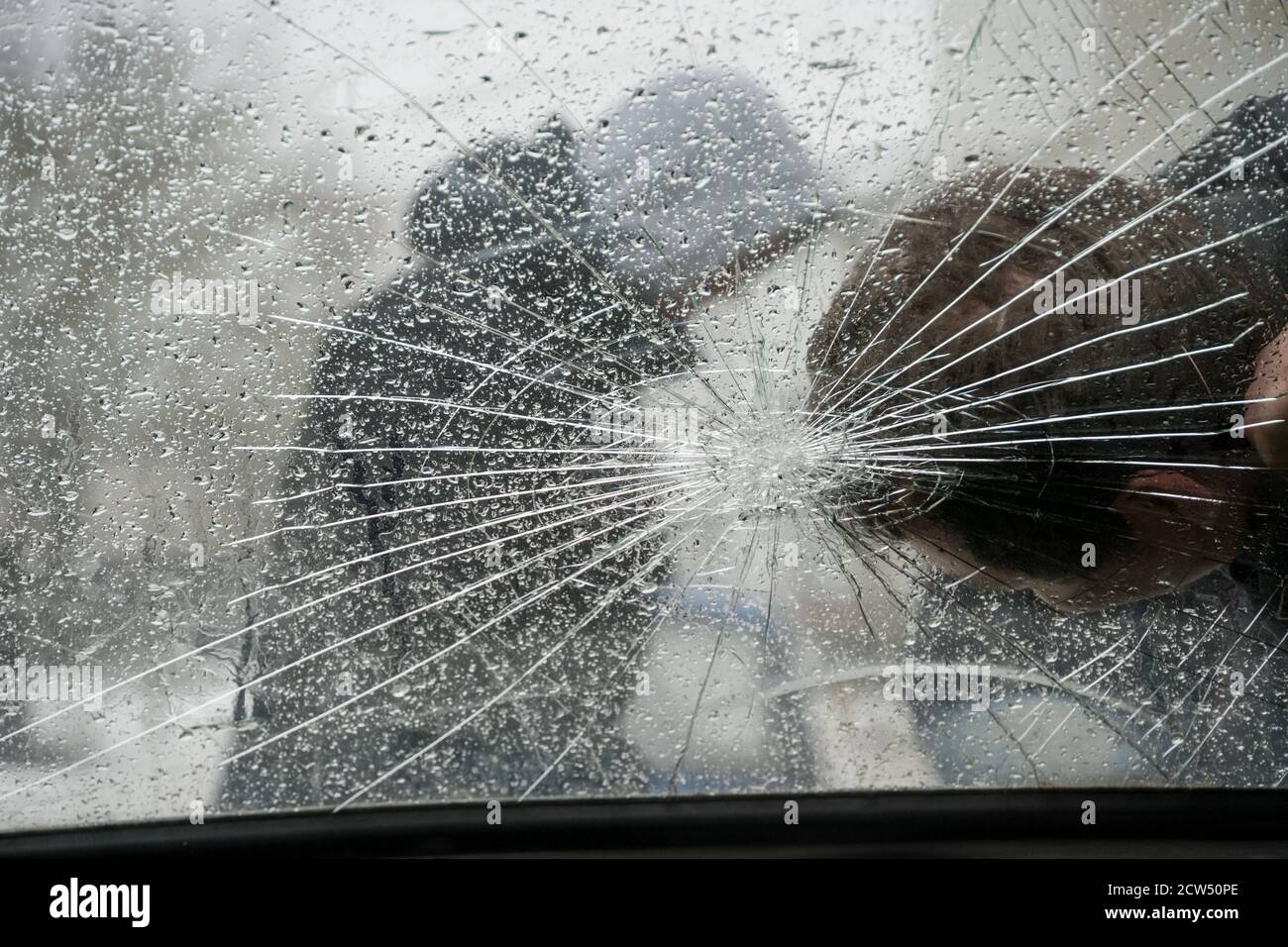 Pedestrian, downed by a car, on a split windshield. The intruder, the thief in the hood. Stock Photo