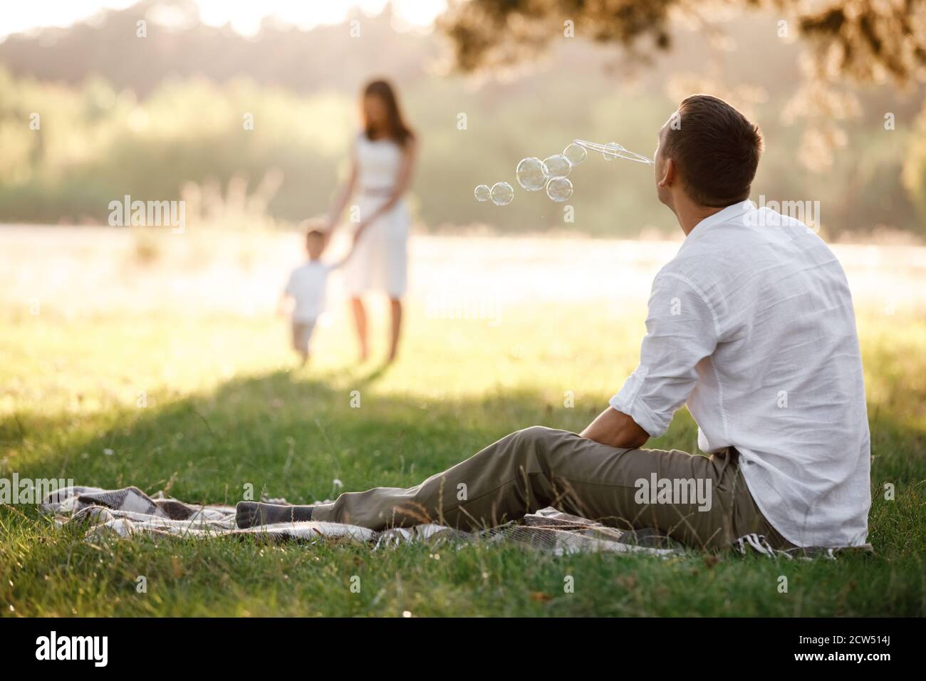father, mother and son blow soap bubbles in the park together on a sunny summer day. happy