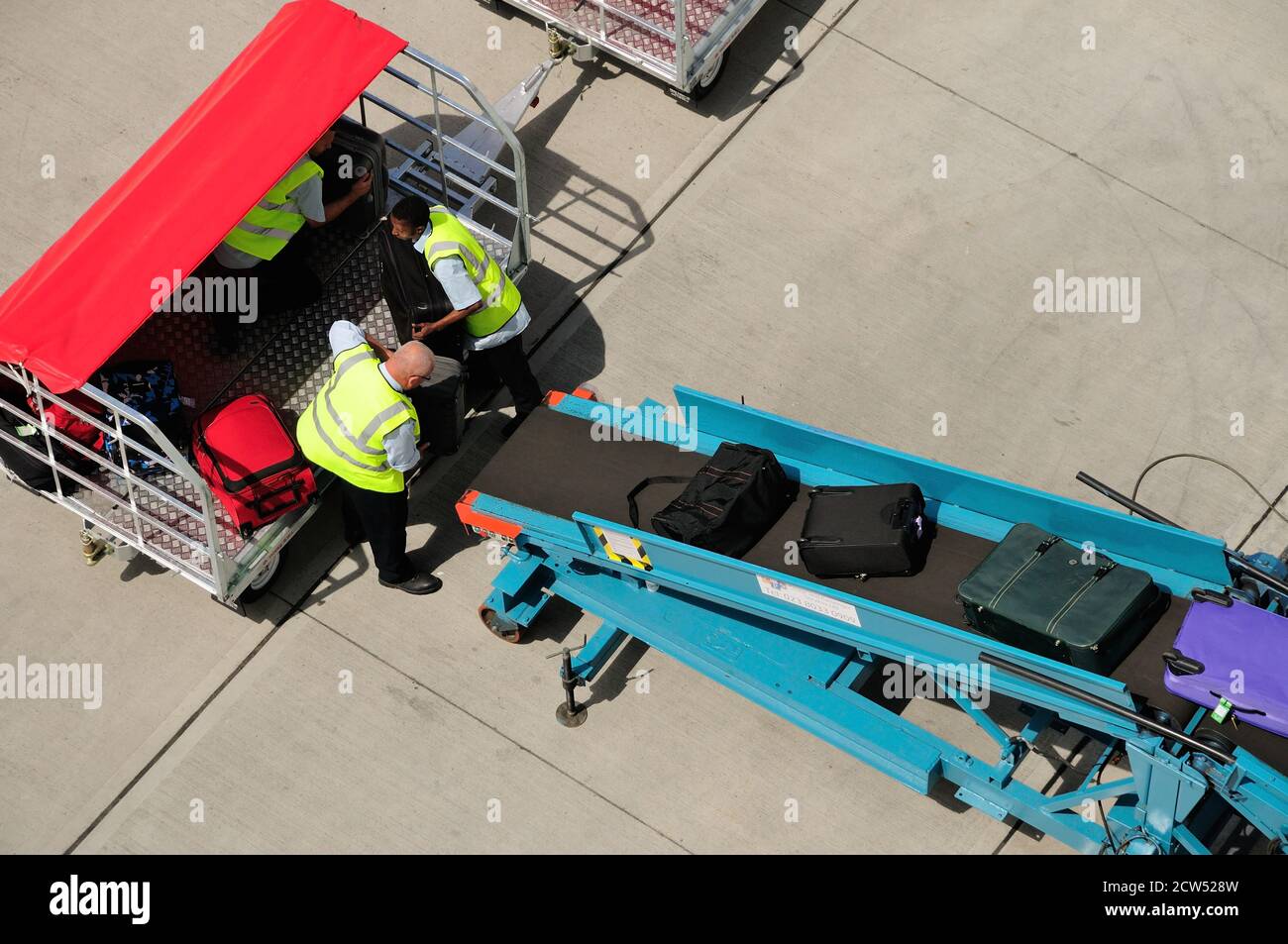 Baggage handlers loading suitcases onto a conveyer belt at a cruise ship terminal in Southampton. Stock Photo