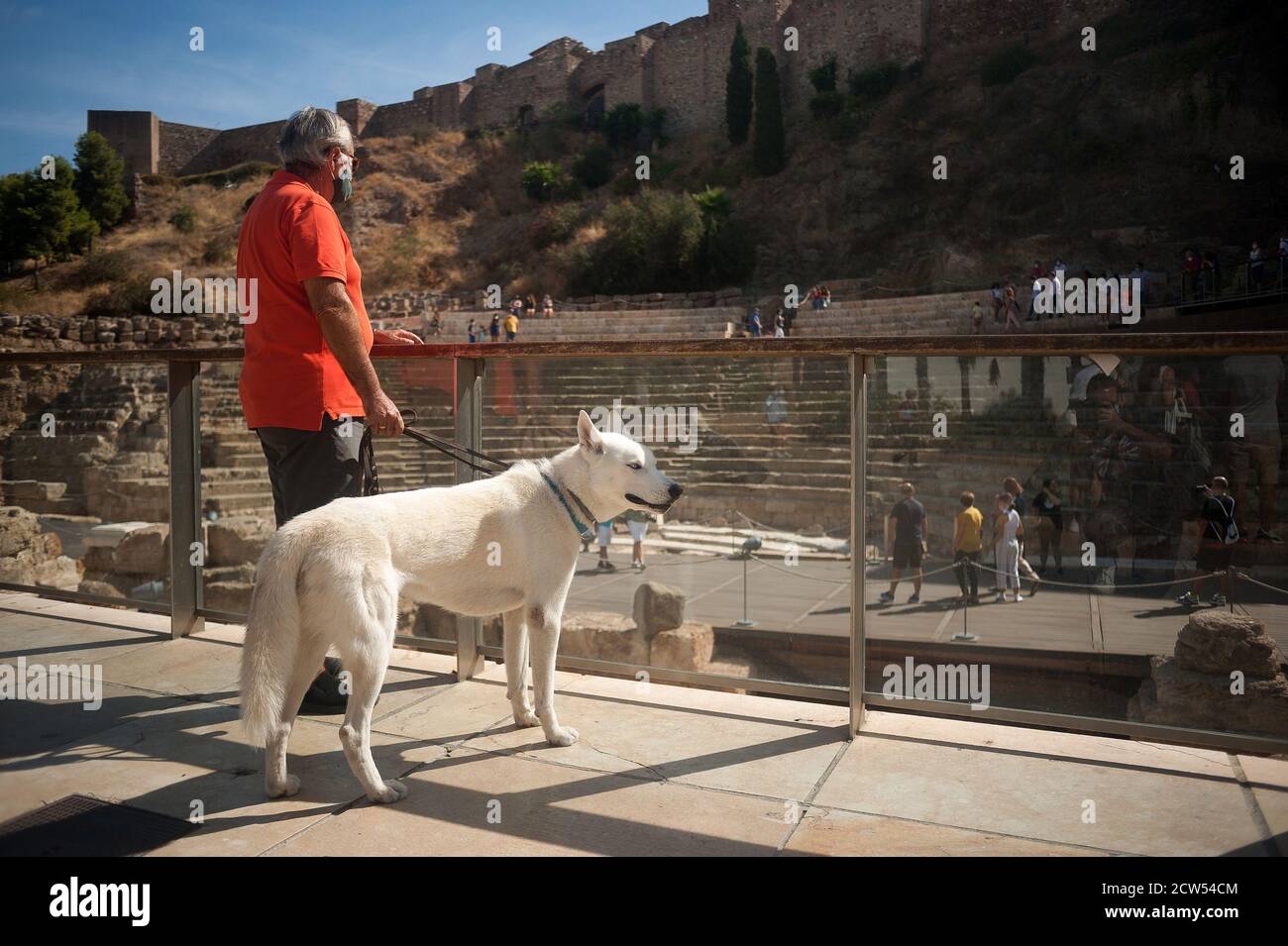A man wearing a face mask seen with his dog in front of roman theatre, part of the moorish fortification known as 'Alcazaba de Málaga', a representative monument from the city during the World Tourism Day.Besides the decrease in international tourism in Andalusia, Malaga celebrates the World Tourism day with an open day in all their museums and representatives monuments, with access and guide visits free for the tourists and citizens. The visits are conducted under safety measures to prevent the spread of coronavirus disease. Stock Photo