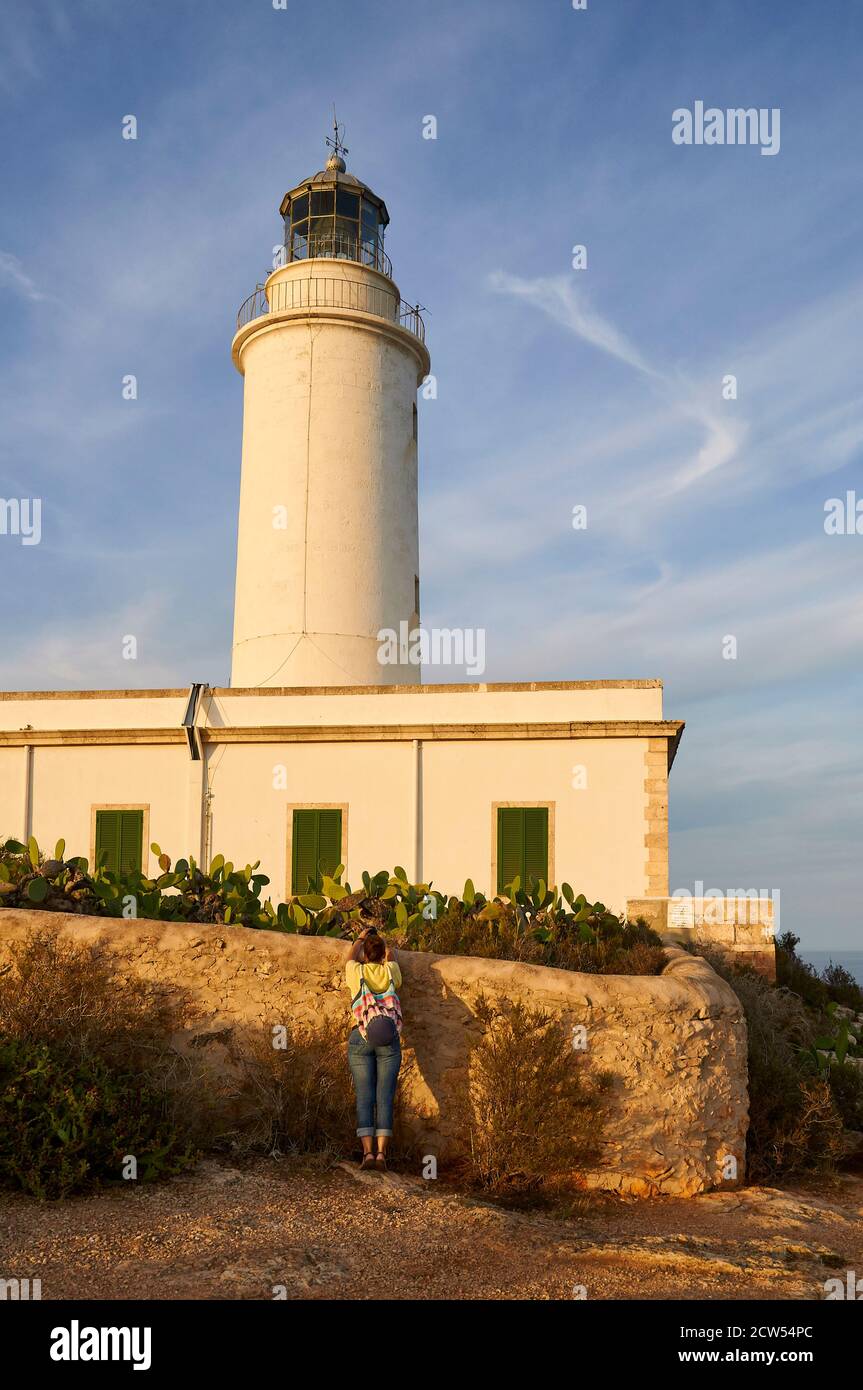 Female hiker photographing Far de La Mola lighthouse against blue sky in a clear day (La Mola, Formentera, Pityusic Islands, Balearic Islands, Spain) Stock Photo