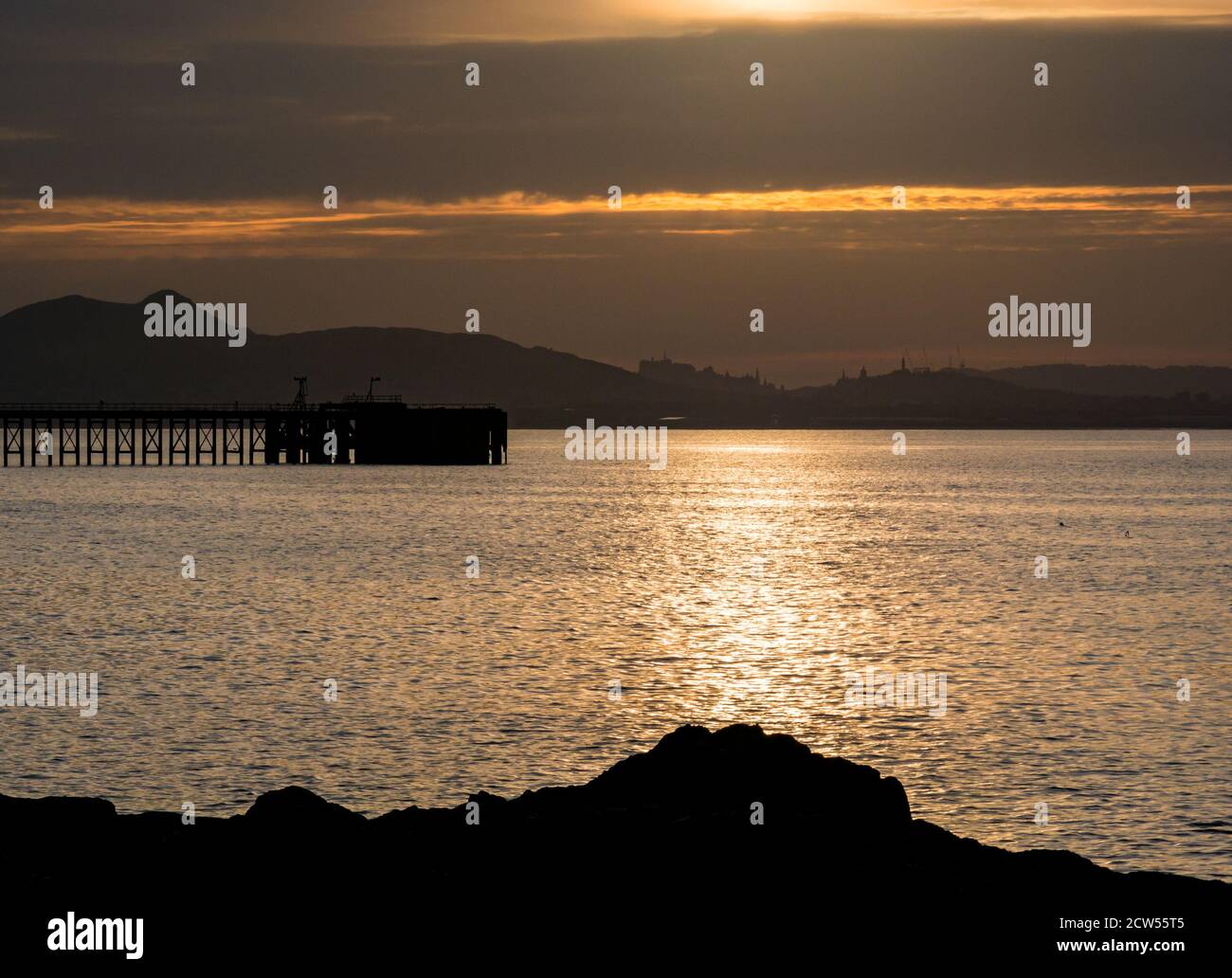 East Lothian, Scotland, United Kingdom, 27th September 2020. UK Weather: sunset over the Firth of Forth looking towards the distinctive Edinburgh skyline with a silhouette of Cockenzie disused pier Stock Photo