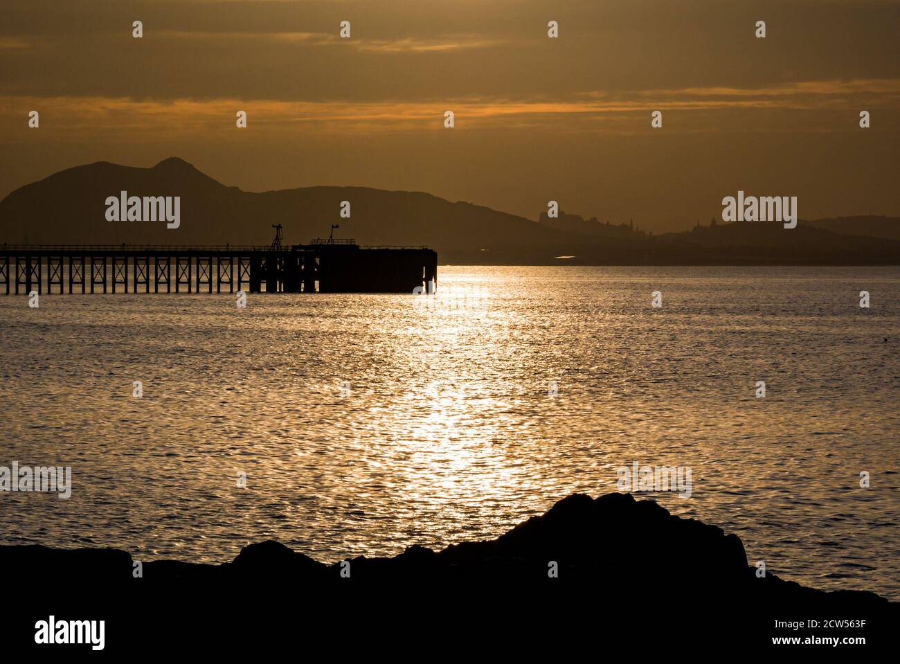 East Lothian, Scotland, United Kingdom, 27th September 2020. UK Weather: sunset over the Firth of Forth looking towards the distinctive Edinburgh skyline with a silhouette of Cockenzie disused pier Stock Photo