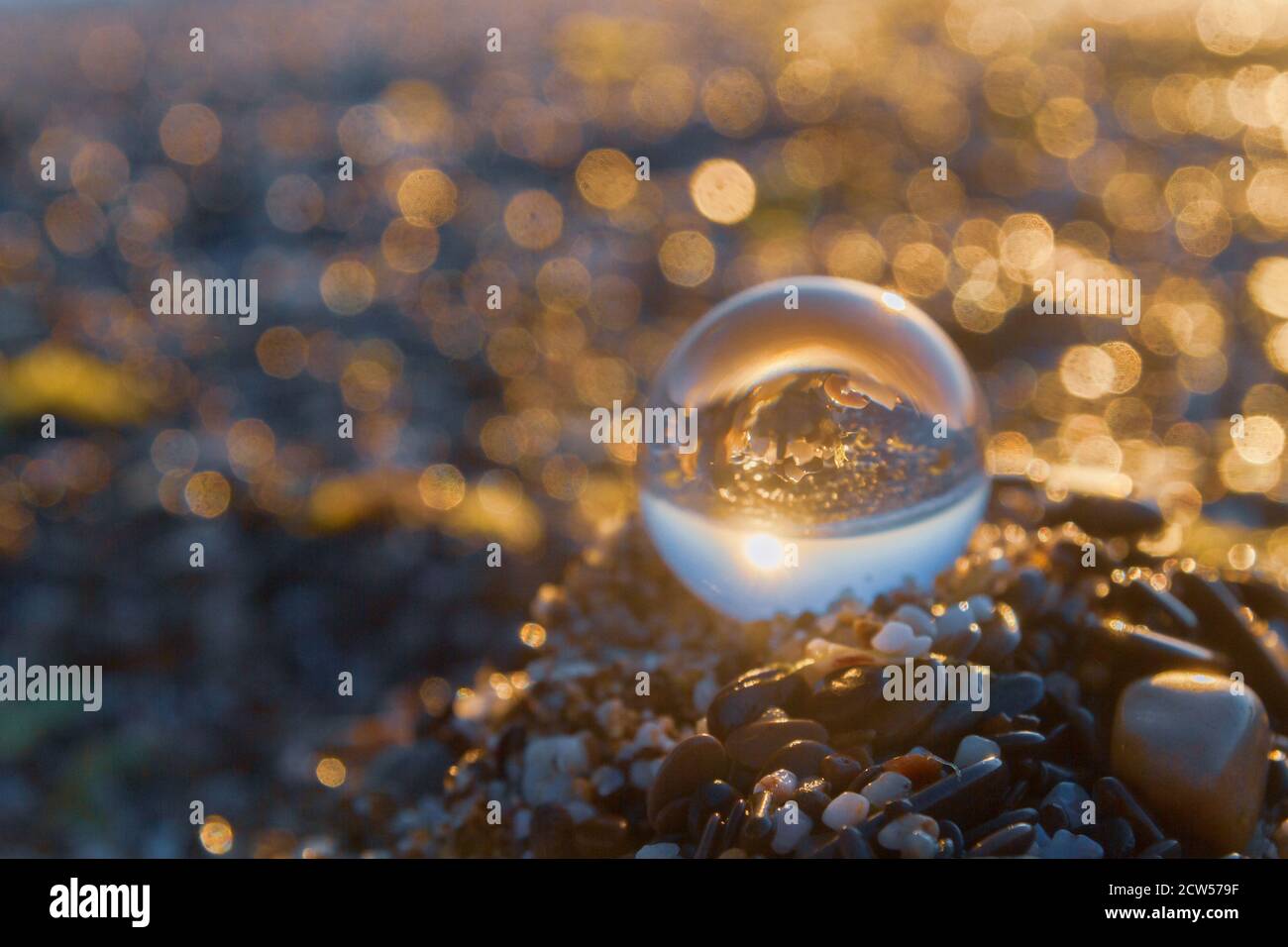 Glass round ball on the beach reflects the sea in summer at sunset ...