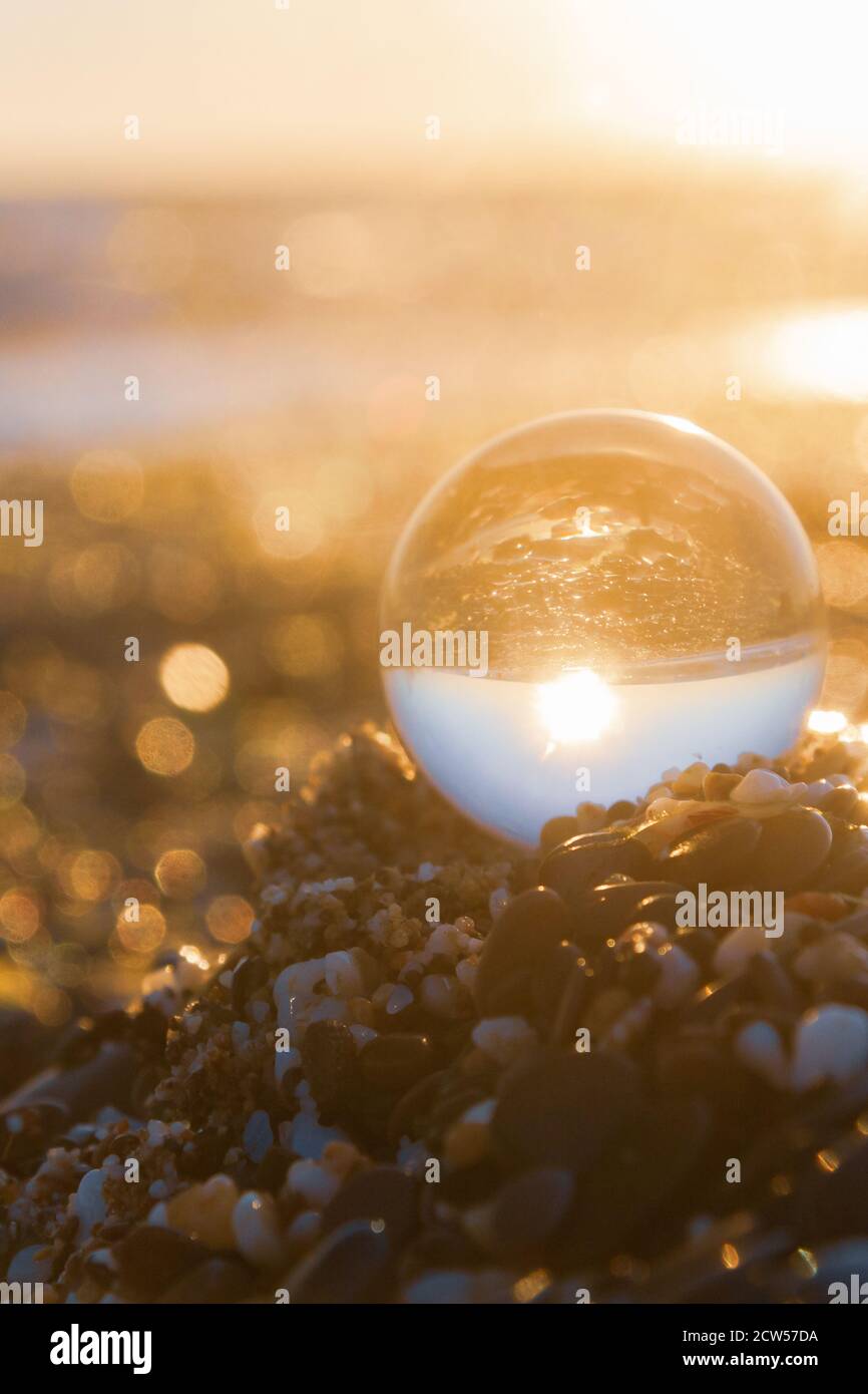 Glass round ball on the beach reflects the sea in summer at sunset ...