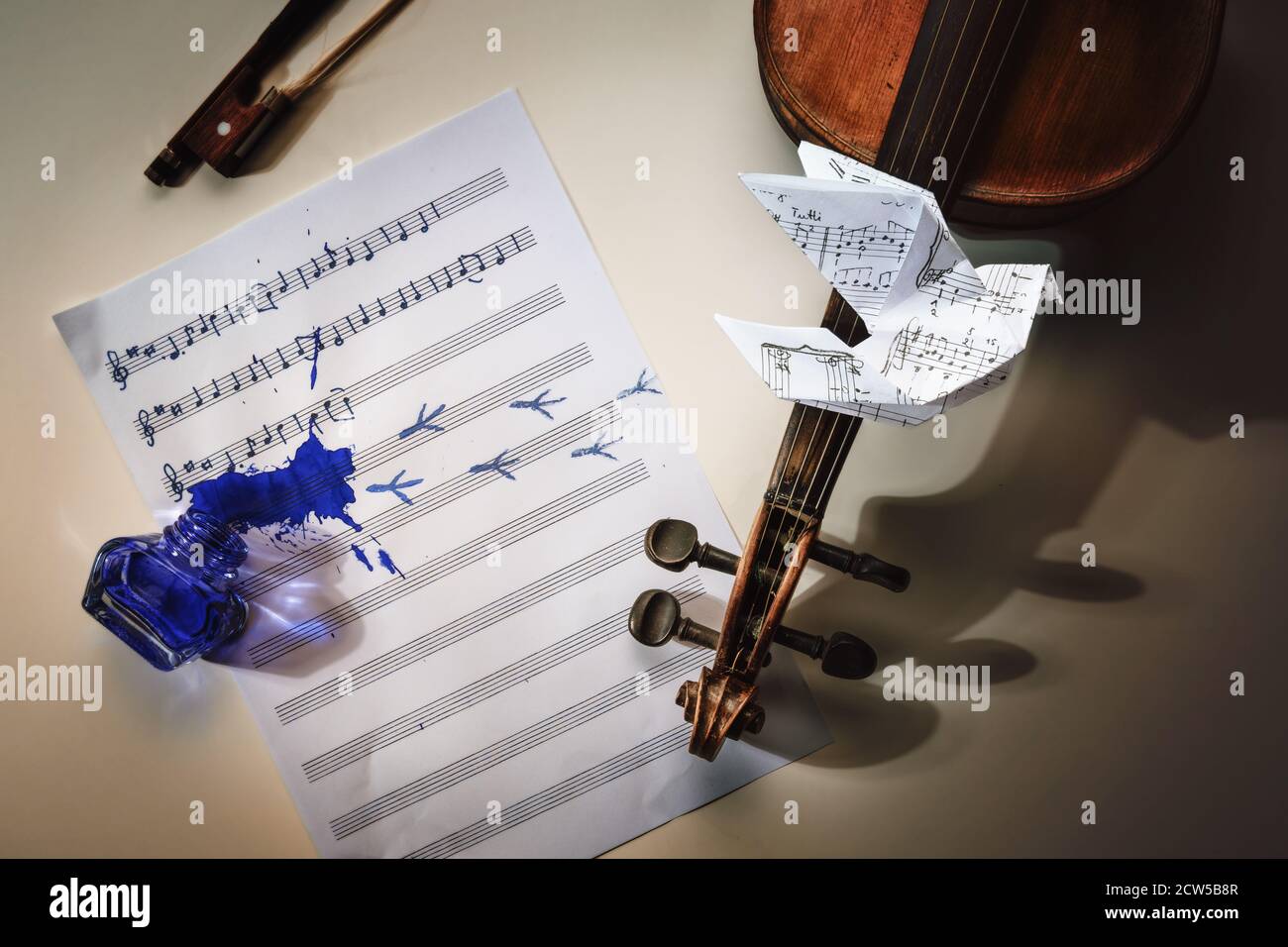 Violin and a sheet of music with started handwritten song All the birds are already here, overturned ink jar, bird footprints and an origami dove flyi Stock Photo